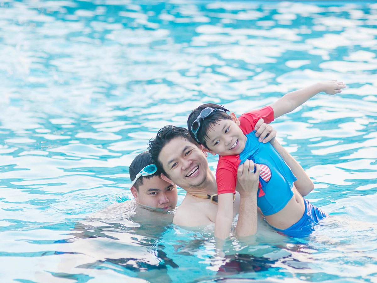 Two men and a boy laughing together in a swimming pool